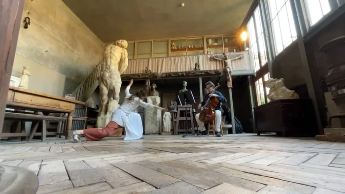 Fente au sol de la danseuse dans l’atelier, le violoncelliste derrière elle
